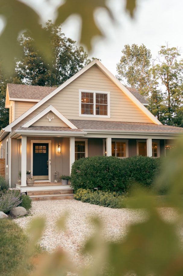 SEARCH MACOMB COUNTY Light-colored house with a dark front door, surrounded by trees and greenery.